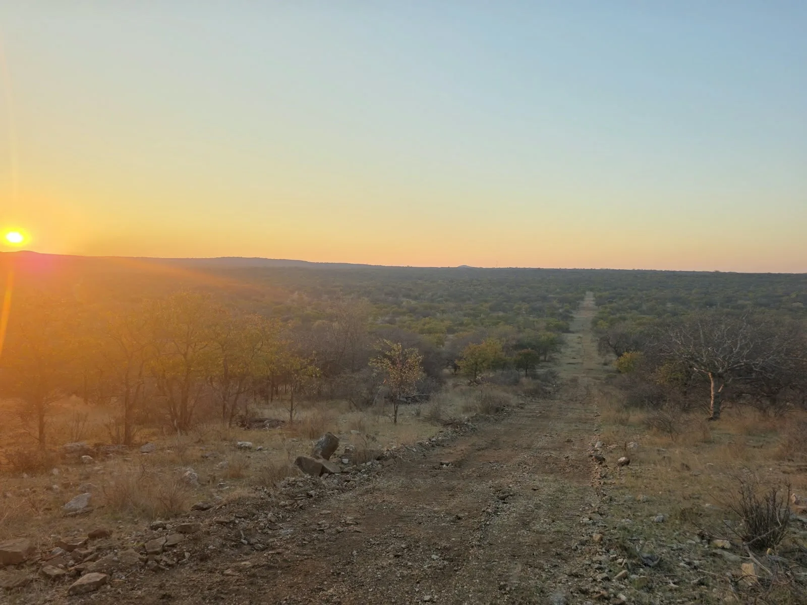 Sun setting over a broad bushveld landscape from a rocky hillside